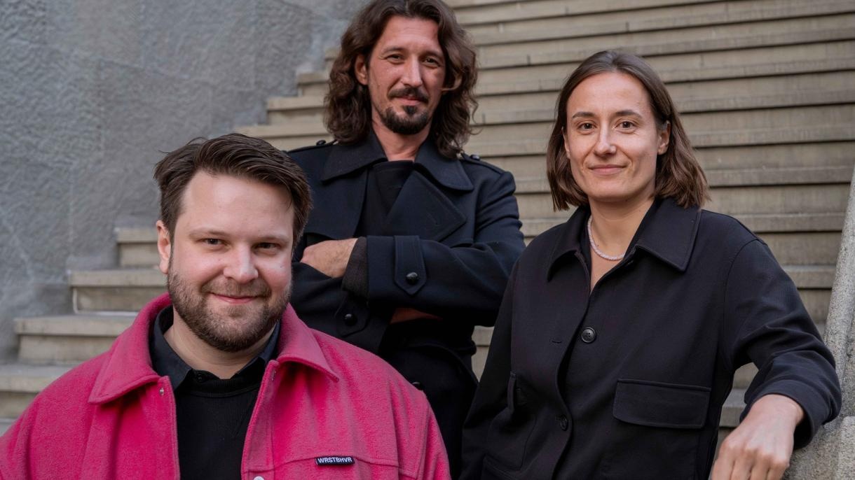 Porträtfoto von drei Personen auf einer Treppe. Zu sehen sind zwei Männer und eine Frau